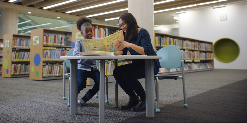 Child and woman reading a book at a table in the library